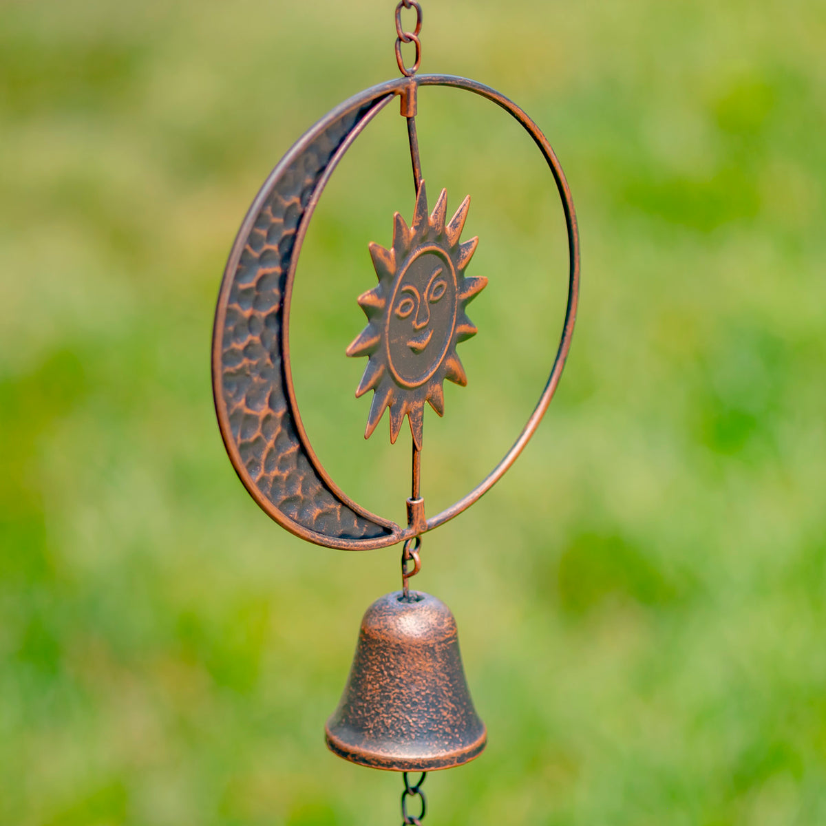 Decorative metal wind chime with sun and moon design against a blurred green background