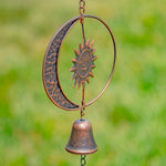 Decorative metal wind chime with sun and moon design against a blurred green background