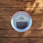 A round metal tin of Wildflower Seed Blend 'Premium Crimson Clover' by Napa Wildflower Co., placed on a rustic wooden plank surface.