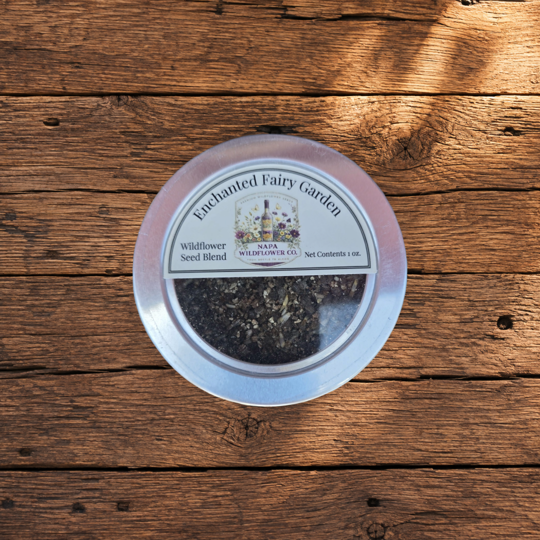 A round metal tin of Napa Wildflower Co. Enchanted Fairy Garden seed blend, displayed on a rustic wooden plank surface.