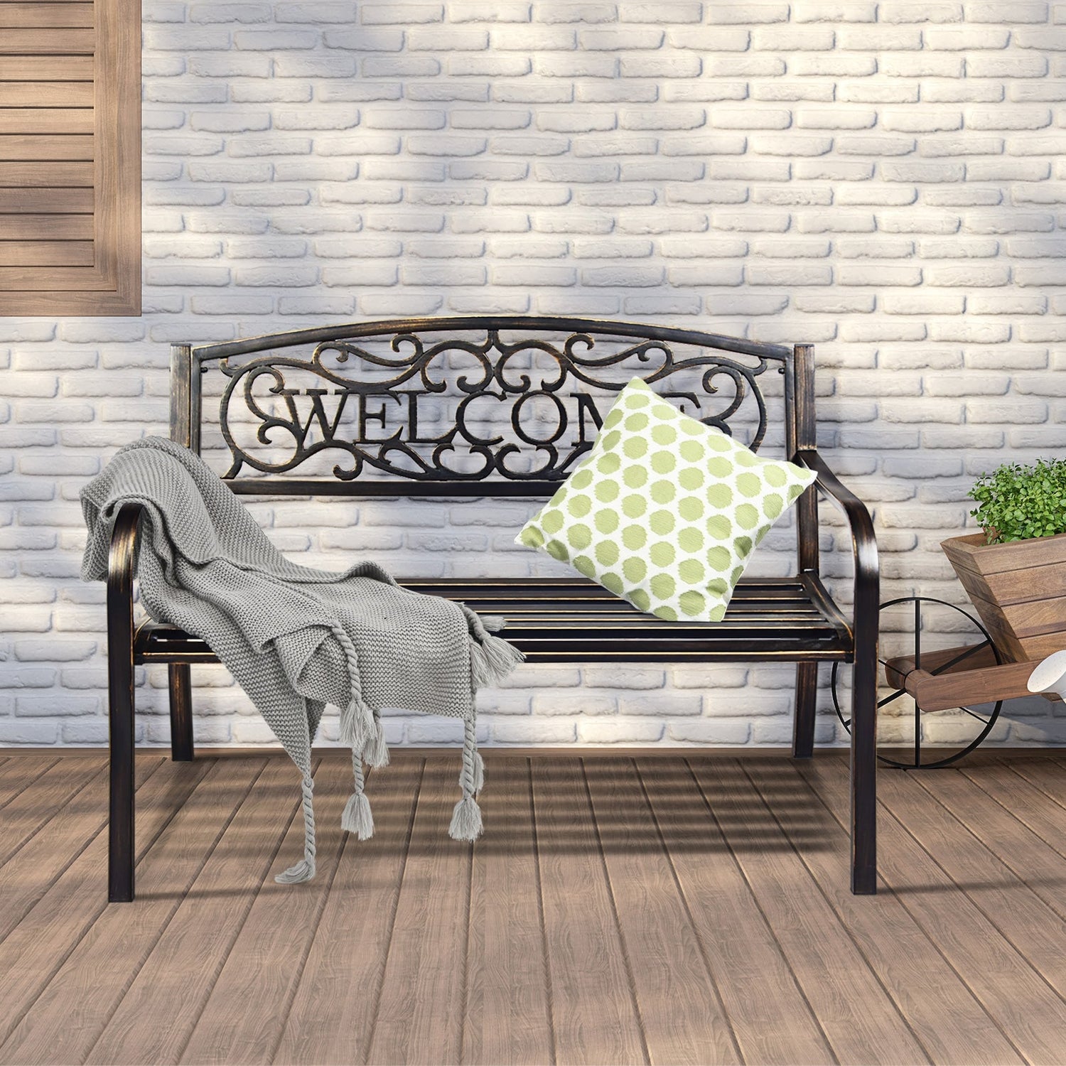 Decorative metal bench with 'WELCOME' text on a wooden deck against a white brick wall.