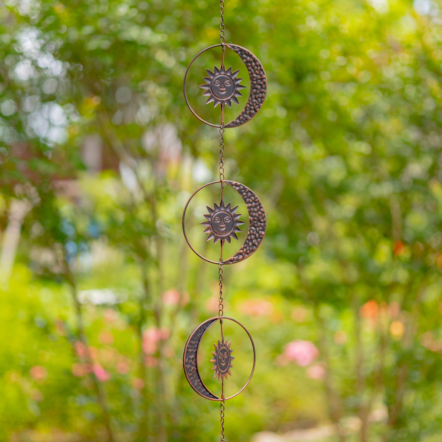 Decorative hanging with sun and moon designs against a blurred green garden background