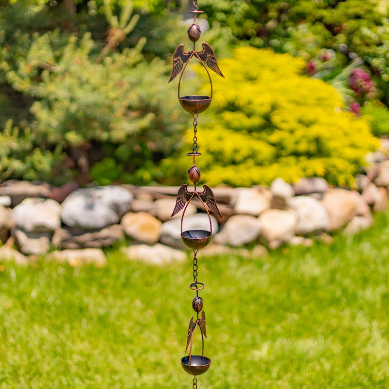 Decorative wind chime with angel designs hanging in a garden setting.