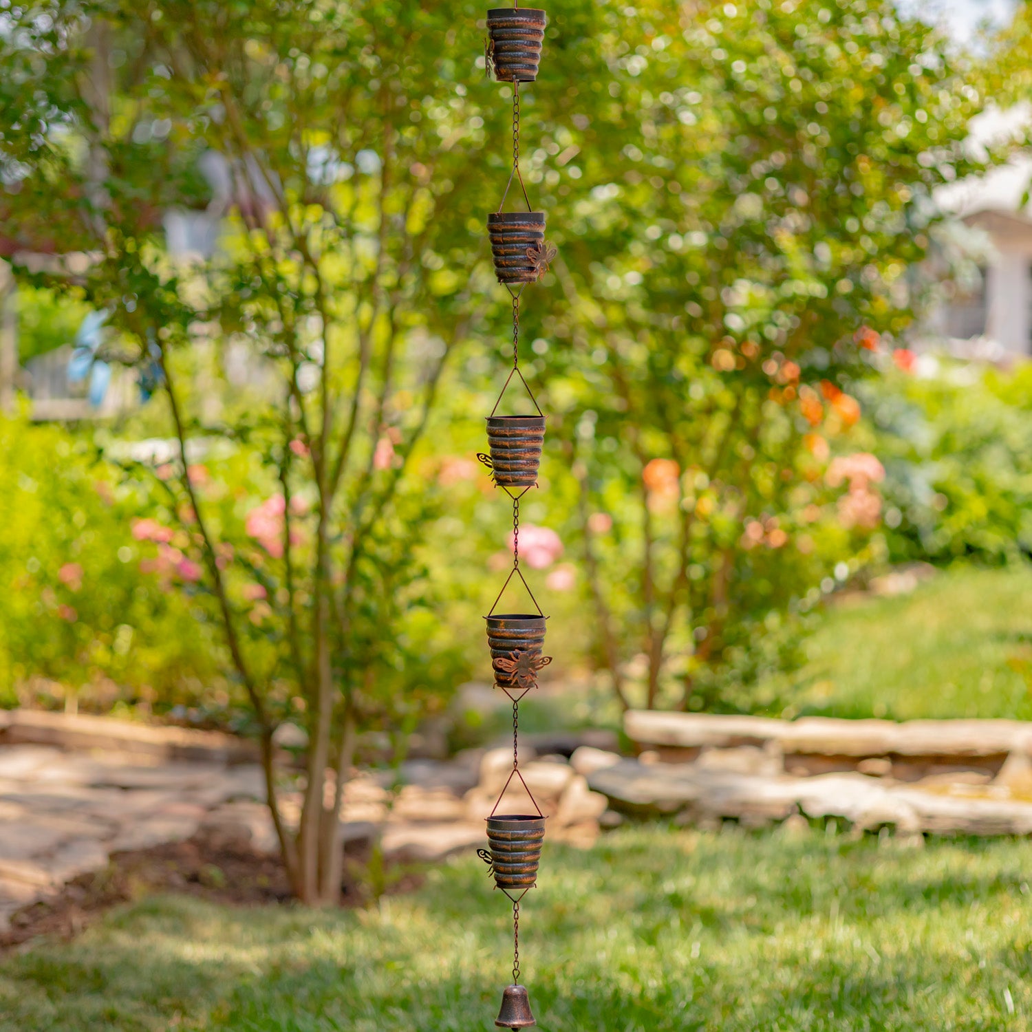 Decorative hanging chime in a garden setting with greenery and a stone path.