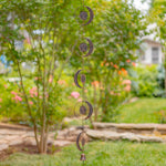 Decorative metal wind chime with sun and moon shapes in a garden setting.