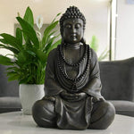 Buddha statue with beads on a table with plants and a couch in the background