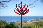 Red decorative garden stake against a scenic background with ocean and sky.