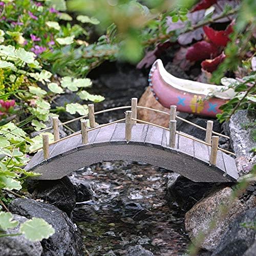 Miniature bridge over a small stream in a garden setting with flowers and rocks.
