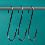 Black S-hooks hanging on a metal rod against a teal background