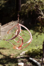 Copper wind chime hanging outdoors with a blurred natural background