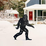 Bigfoot silhouette in front of a house with a snowy landscape