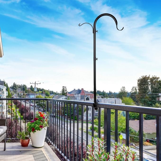Black metal plant hanger on a balcony railing with a scenic view of houses and trees.