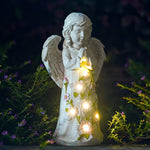Decorative angel statue with string lights and flowers against a dark background