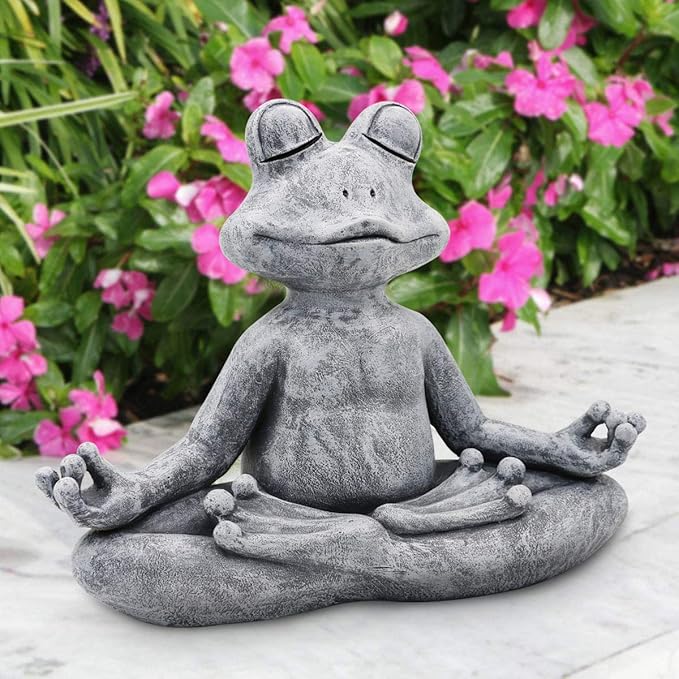 Gray frog statue in a meditating pose with pink flowers in the background