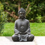 Statue of a meditating Buddha in a garden setting with greenery.