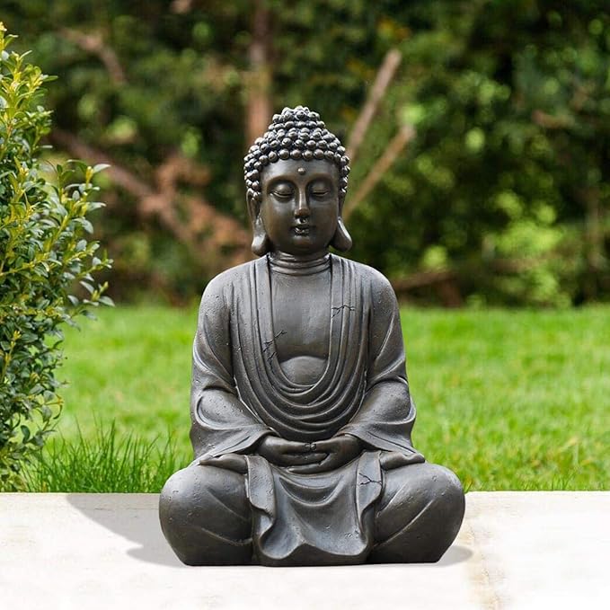 Statue of a meditating Buddha in a garden setting with greenery.