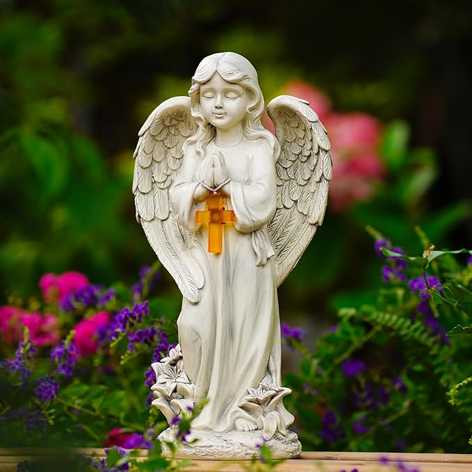 Statue of an angel holding a cross in a garden setting with flowers.