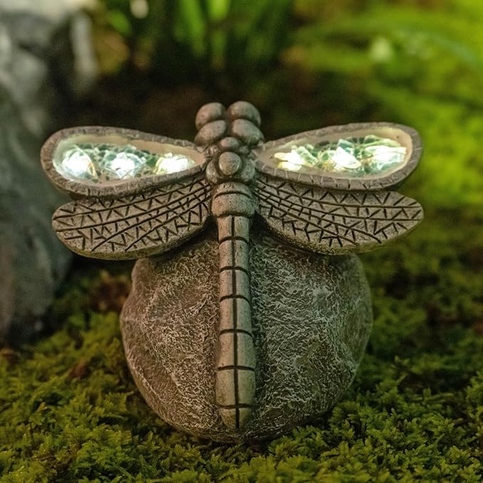 Decorative dragonfly sculpture with solar lights on a mossy surface
