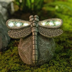 Decorative dragonfly sculpture with solar lights on a mossy surface