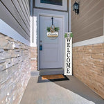 Front door of a house with a welcome mat and a large vertical welcome sign.