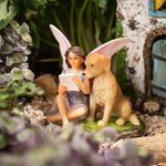 Fairy figurine with a teddy bear reading a book in a miniature garden setting.