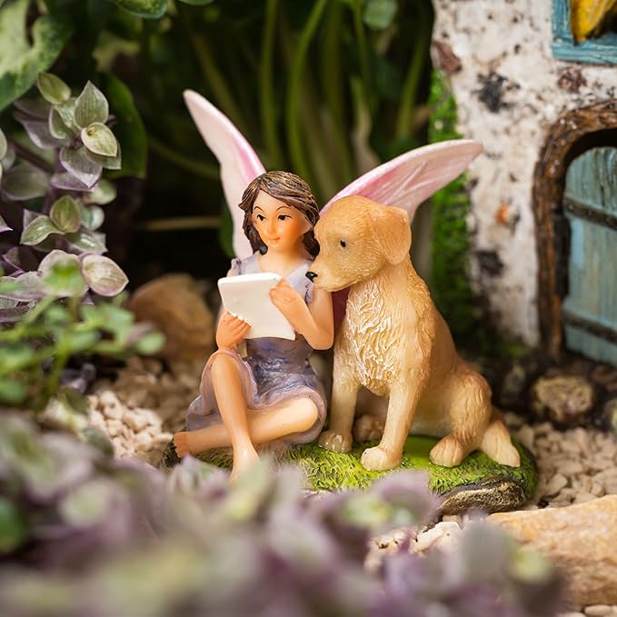 Fairy figurine with a teddy bear reading a book in a miniature garden setting.