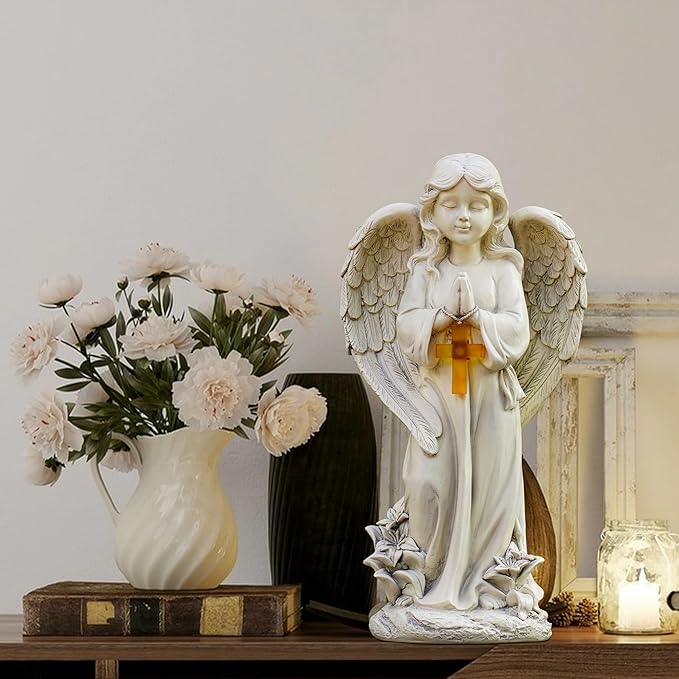 Statue of an angel holding a candle next to a vase of flowers on a wooden surface.