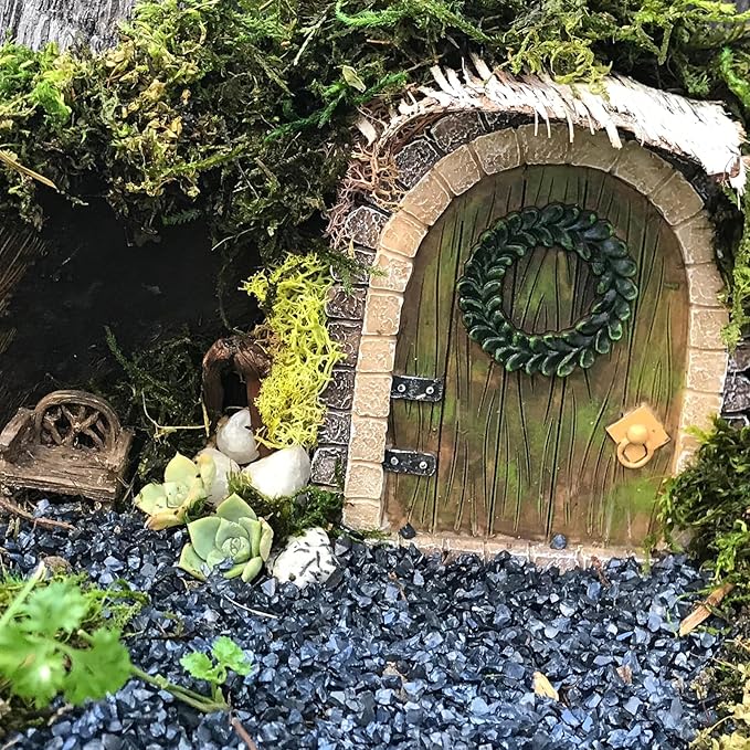 Miniature fairy door with wreath surrounded by greenery and small plants