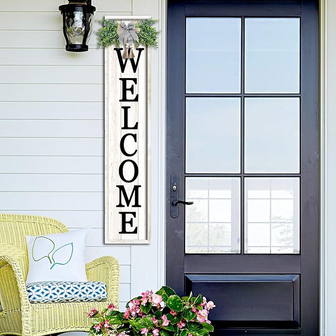 Front door with a 'WELCOME' sign, chair, and flowers on a white wall.