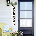 Front door with a 'WELCOME' sign, chair, and flowers on a white wall.