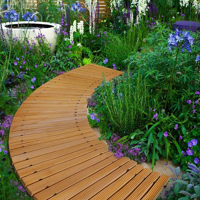 Wooden garden path winding through a lush garden with flowers and plants.
