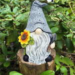 Gnome figurine with a sunflower on a wooden stump surrounded by greenery