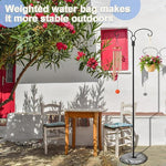 Outdoor setting with a table and chairs under a tree with red flowers, and a standing lamp with a weighted water bag.
