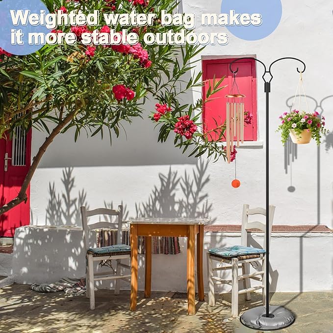 Outdoor setting with a table and chairs under a tree with red flowers, and a standing lamp with a weighted water bag.