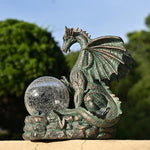 Bronze dragon statue with a crystal ball on a stone base against a blurred natural background