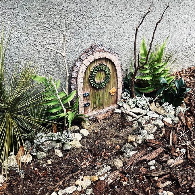 Miniature fairy door in a garden setting with plants and stones.