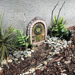 Miniature fairy door in a garden setting with plants and stones.