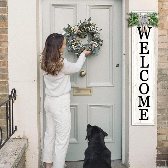 Woman placing a wreath on a door with a dog looking up, and a 'WELCOME' sign to the right.