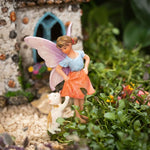 Fairy figurine with a dog in front of a miniature house in a garden setting