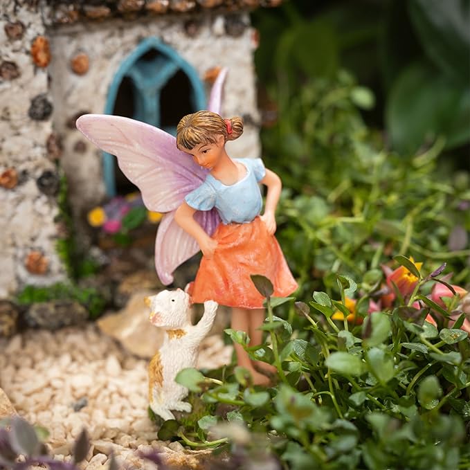 Fairy figurine with a dog in front of a miniature house in a garden setting