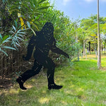 Black silhouette of a gorilla against a natural background with trees and grass.