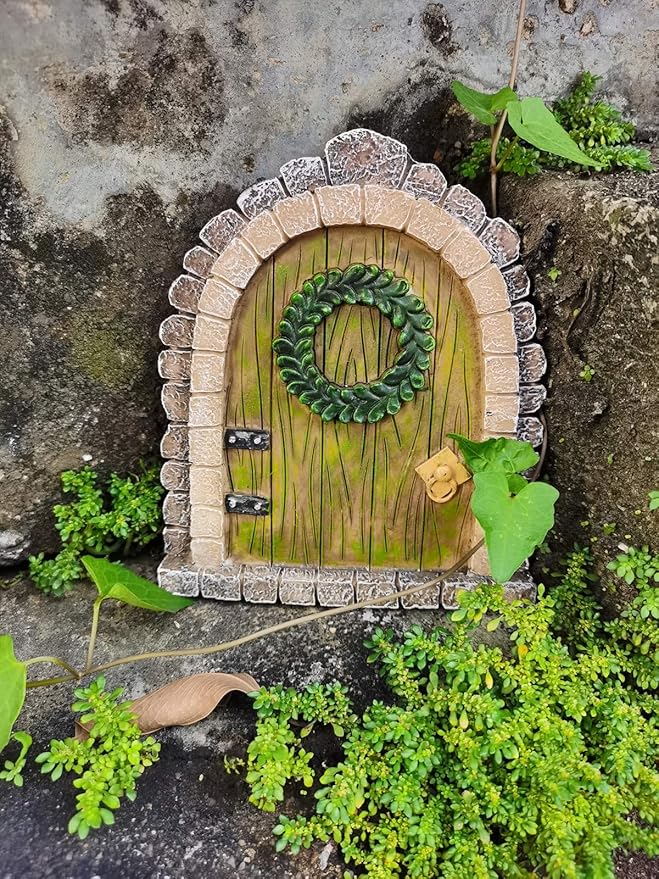 Miniature stone archway with a green door and wreath, surrounded by plants on a rocky background.