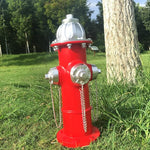 Red fire hydrant with silver components on a grassy area with trees in the background