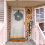 Front door with wreath, welcome sign, and doormat on a house exterior.