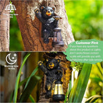 Bear figurine with a lantern on a tree trunk, surrounded by greenery.