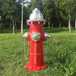 Red fire hydrant with silver components on a grassy area with trees in the background