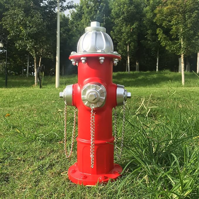 Red fire hydrant with silver components on a grassy area with trees in the background