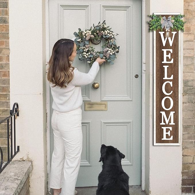 Woman placing a wreath on a door with a 'WELCOME' sign and a dog watching.