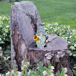 Gnome figurine with a sunflower on a wooden stump in a garden setting