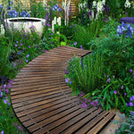 Wooden garden path winding through a lush garden with flowers and plants.